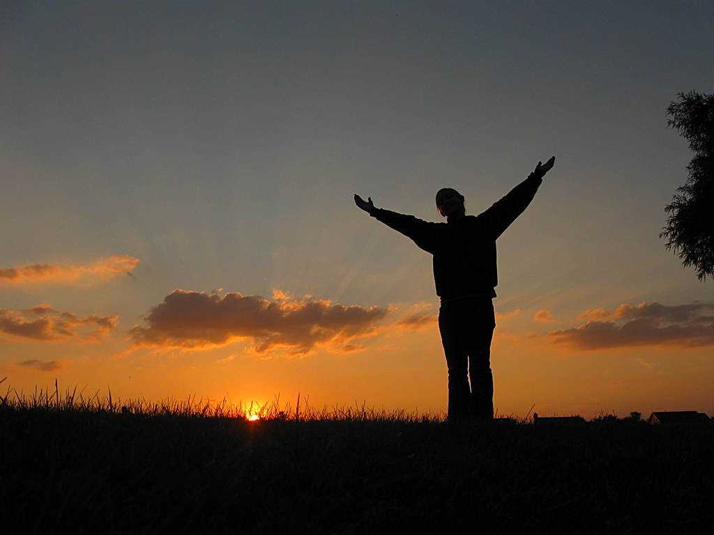 A person standing alone in a field with arms outstretched.